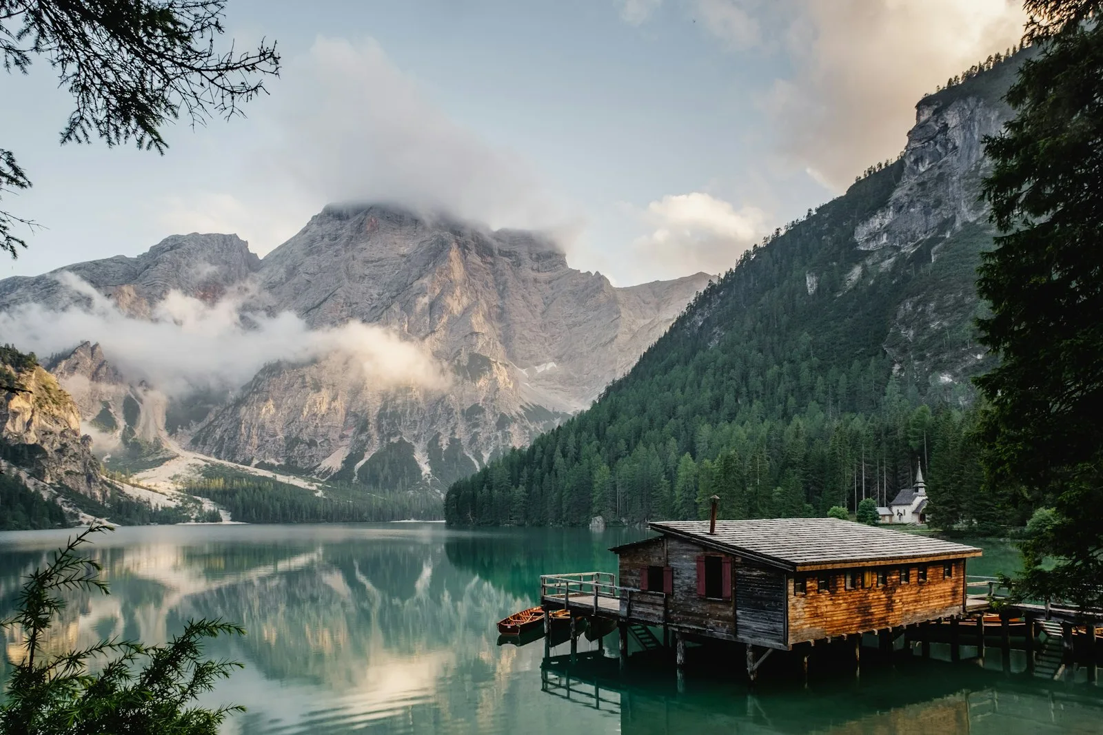 A still alpine lake reflecting mountains and a wooden boathouse.